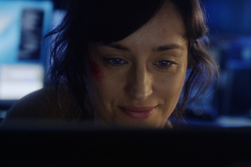 Joven mujer observa pantalla de computadora con expresión concentrada en escena nocturna iluminada azul