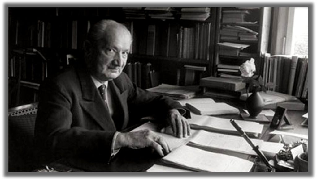 Martin Heidegger en su escritorio rodeado de libros y documentos, escribiendo en blanco y negro