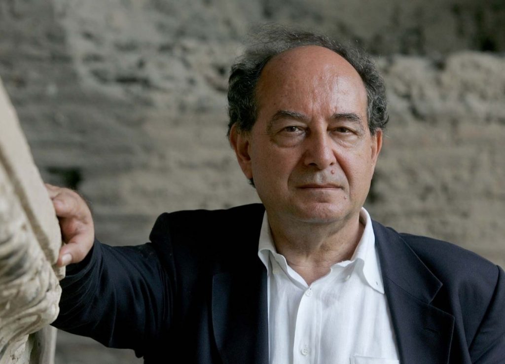 Roberto Calasso, escritor italiano con traje oscuro y camisa blanca, en ambiente exterior con muro de piedra