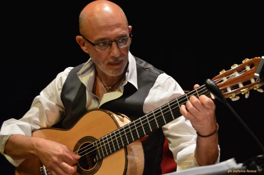 Stefano Macrillò toca guitarra acústica con concentración durante una presentación en escenario oscuro