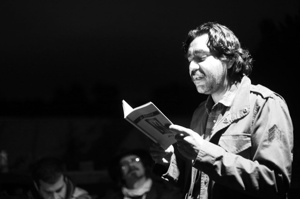 Hombre leyendo desde un podio en blanco y negro, enfocado en su texto bajo luz de escena teatral