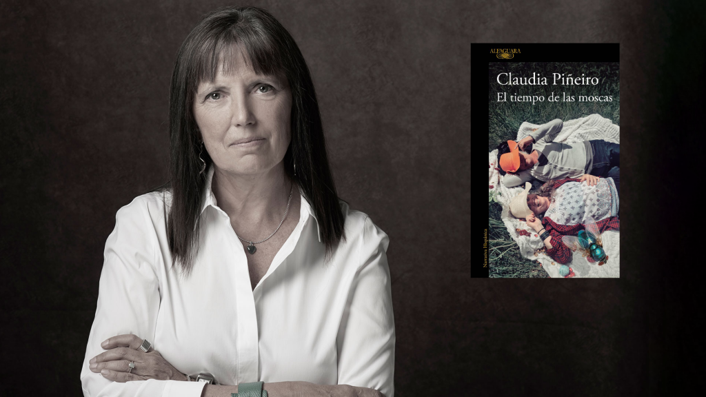 Claudia Piñeiro, autora argentina, posa con los brazos cruzados junto a la portada de El tiempo de las moscas
