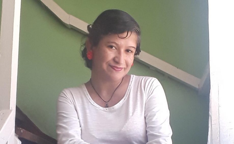 Jessenia Chamorro sonríe frente a una pared verde, vistiendo camiseta blanca en ambiente interior