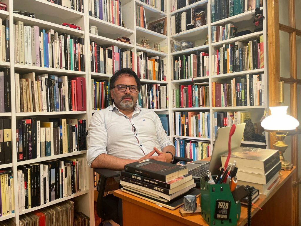 Juan Pablo Belair en su biblioteca personal, sentado ante un escritorio de madera con libros apilados y utensilios