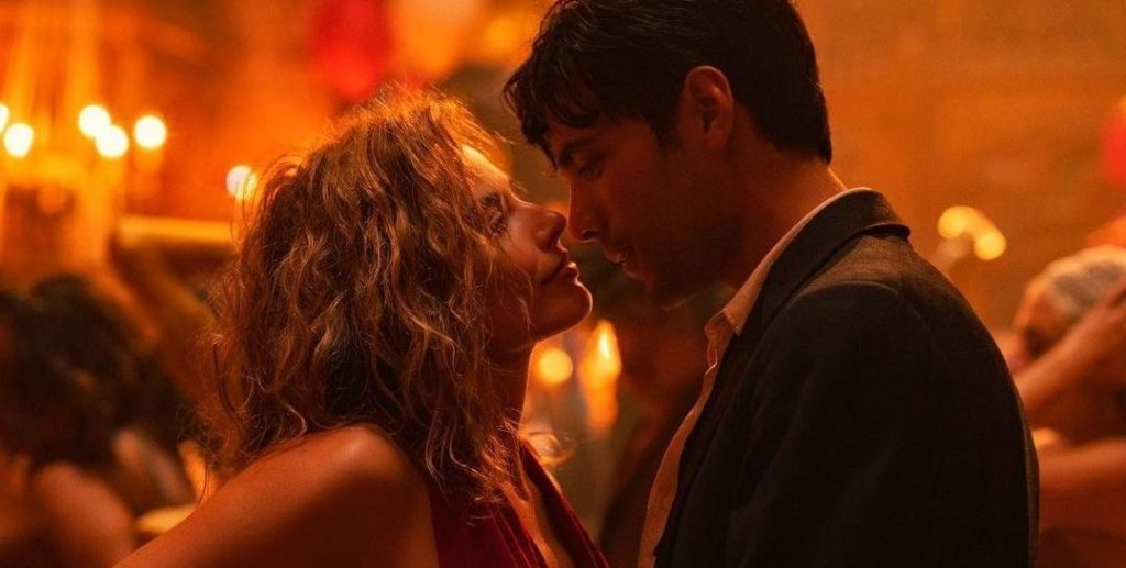 Pareja besándose en ambiente cálido con luces doradas de fondo, escena de intimidad romántica en atmósfera nocturna