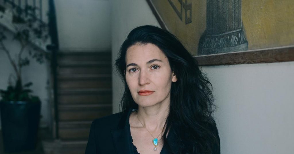 Nicole Krauss, escritora de cabello oscuro y largo, viste chaqueta negra en interior con escaleras de fondo