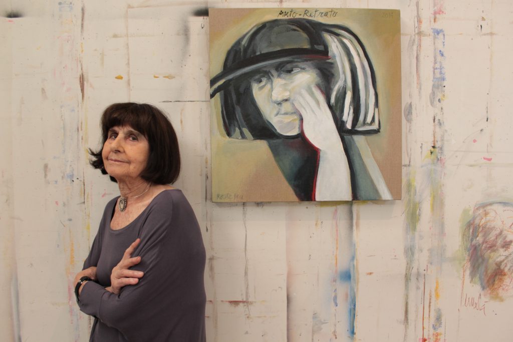Roser Bru junto a su obra, retrato en blanco y negro de una mujer con sombrero, en estudio con paredes blancas