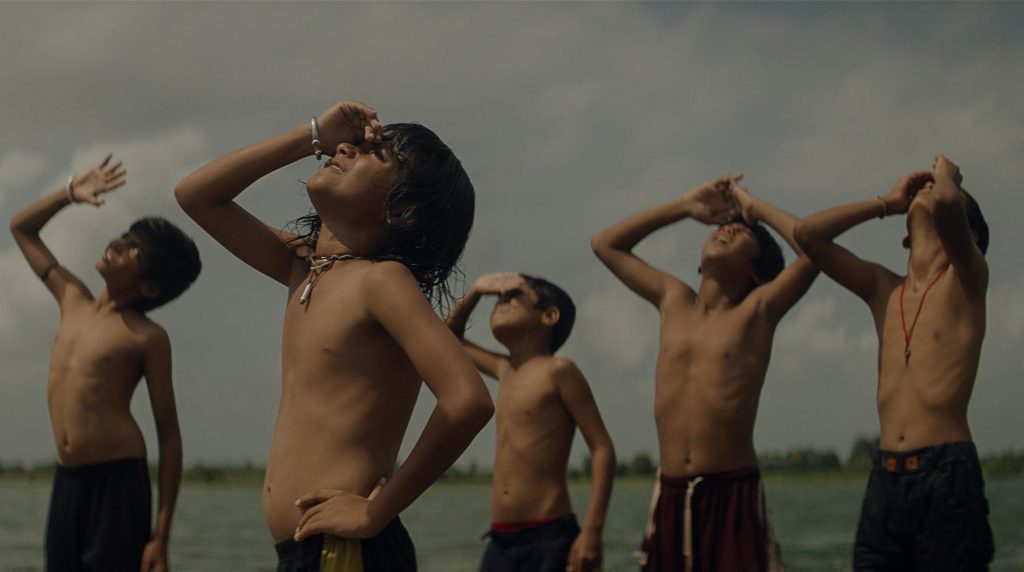 Cinco niños sin camisa observan el cielo junto al mar bajo un firmamento nublado