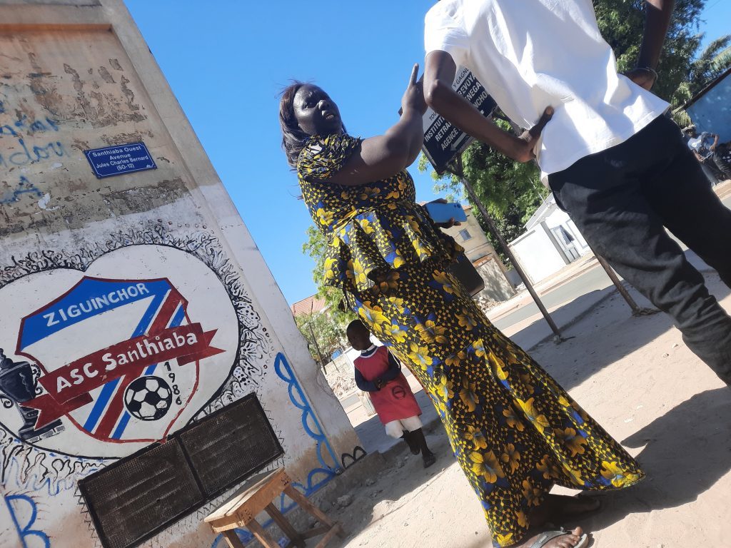 Poeta levanta bandera blanca frente a monumento en plaza de Ziguinchor, Senegal, bajo cielo despejado