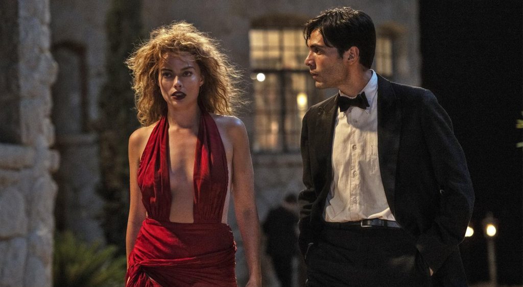 Mujer en vestido rojo y hombre en traje de gala caminan juntos por una calle nocturna de época