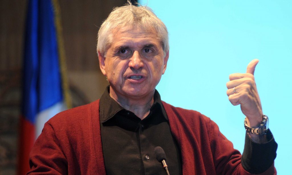 Eugenio Tironi, sociólogo chileno, con camisa roja durante conferencia, gesticulando con pulgar hacia arriba