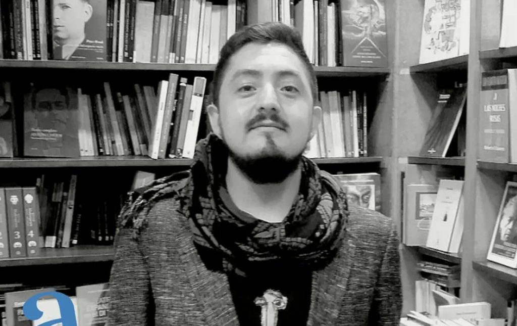 Guido Arroyo, escritor, en primer plano frente a estantería con libros al fondo, en blanco y negro