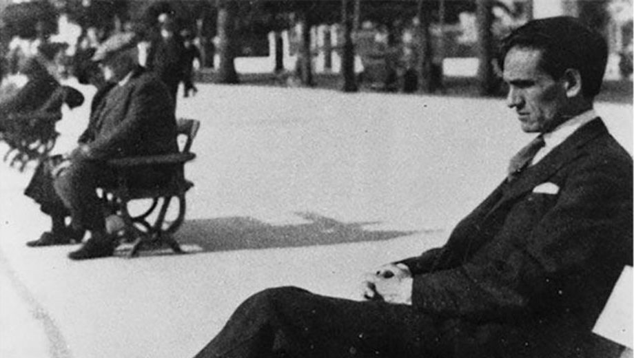 César Vallejo sentado en traje oscuro durante una sesión de filmación, observando la cámara de cine en estudio
