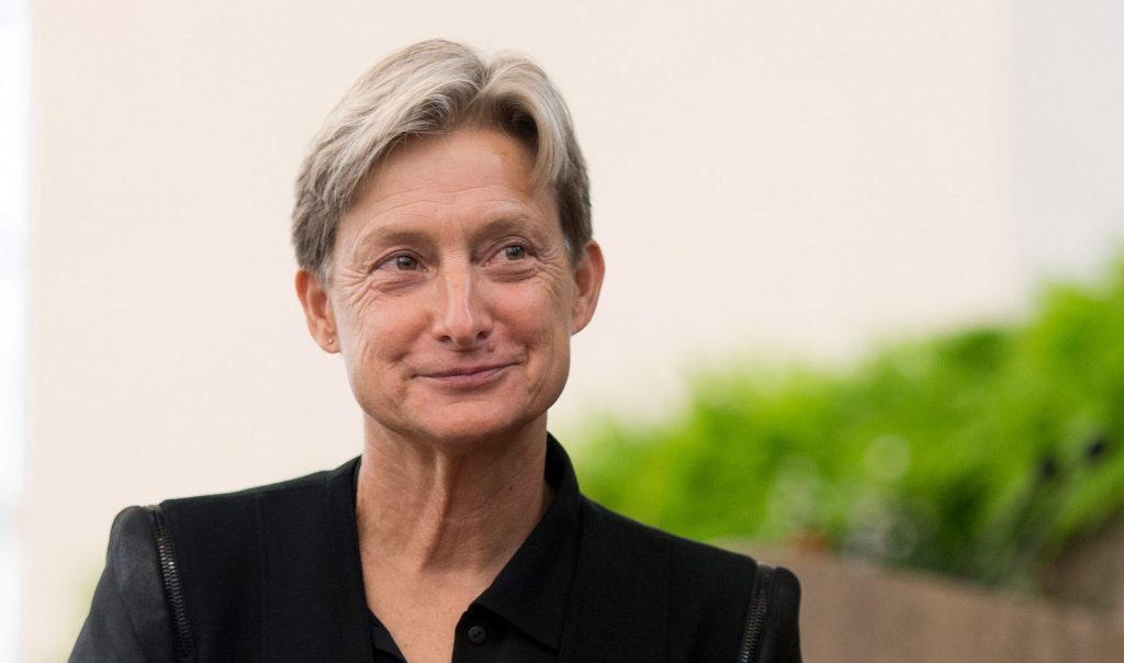 Judith Butler, filósofa estadounidense, sonríe ante cámara vistiendo chaqueta negra sobre fondo desenfocado