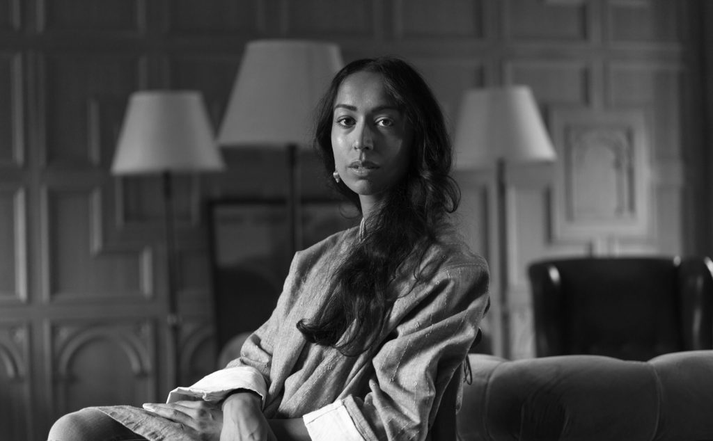 Amia Srinivasan, filósofa, sentada en un sofá dentro de un espacio interior iluminado en blanco y negro