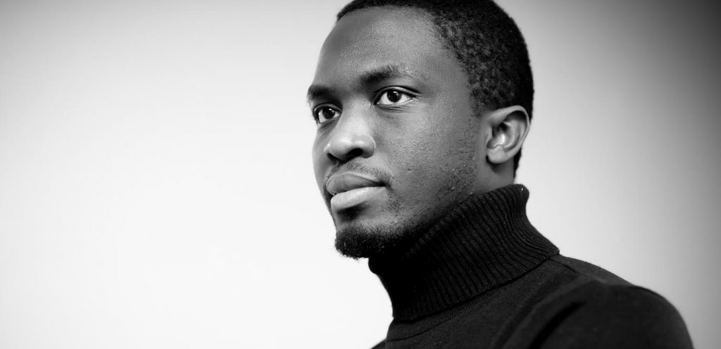 Retrato en blanco y negro del escritor senegalés Mohamed Mbougar Saar, de perfil hacia la derecha, vistiendo cuello