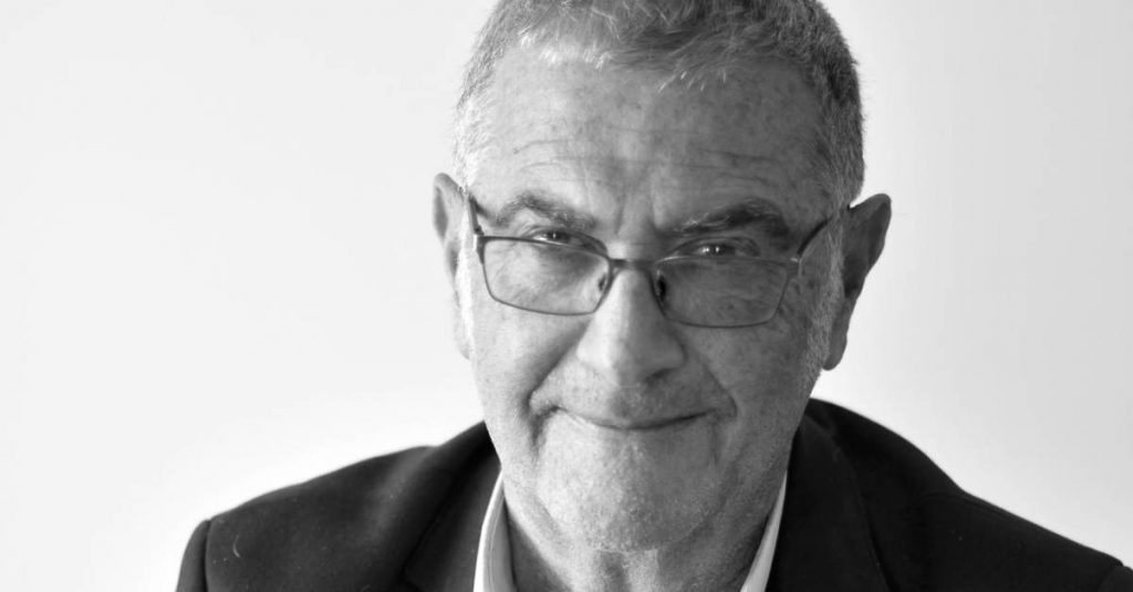 Serge Haroche, hombre de cabello gris y gafas, sonríe ante la cámara con traje oscuro