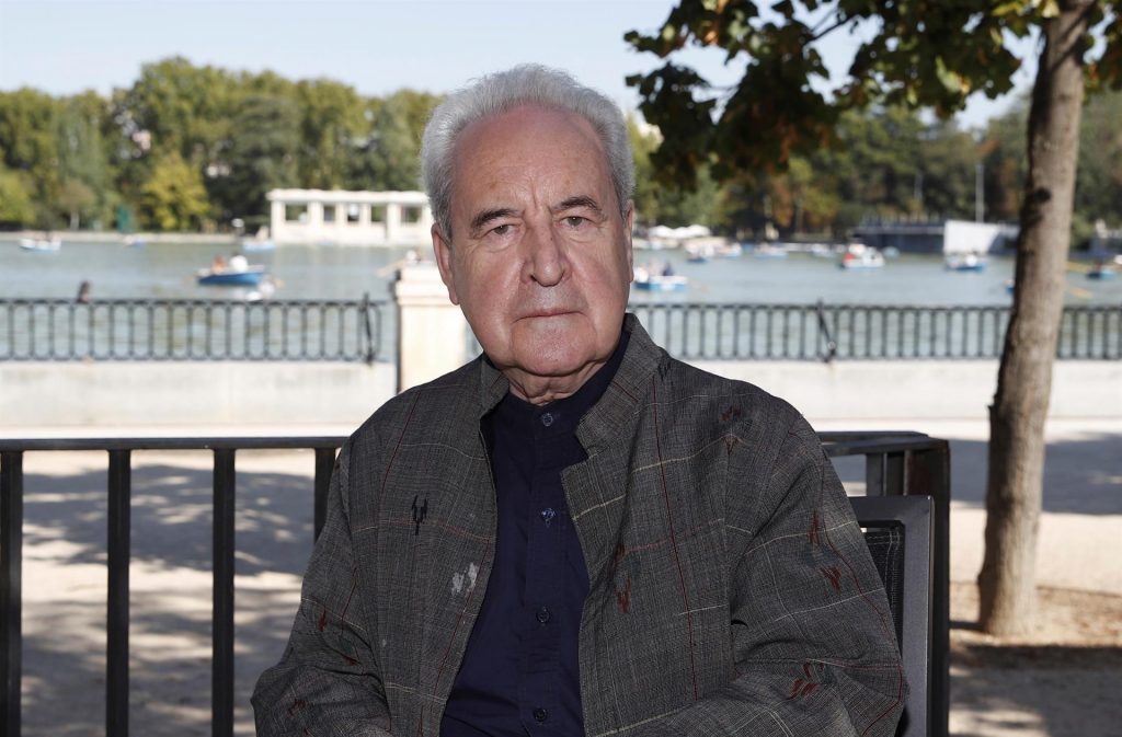 John Banville, escritor irlandés de cabellos grises, sentado en banco junto al agua, con chaqueta oscura