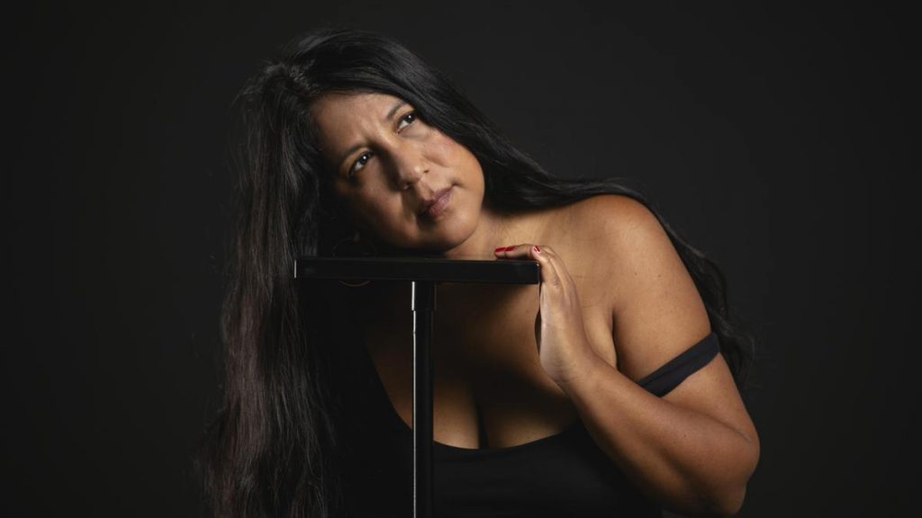 Gabriela Weiner, mujer de cabello largo negro, posa contra fondo oscuro con expresión contemplativa y mano cerca