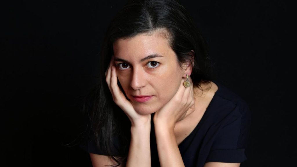 Samanta Schweblin, escritora argentina, apoya su rostro en las manos con expresión reflexiva sobre fondo negro