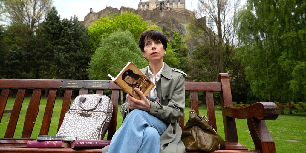 Persona sentada en banco de madera roja con libro y paisaje verde de castillo al fondo