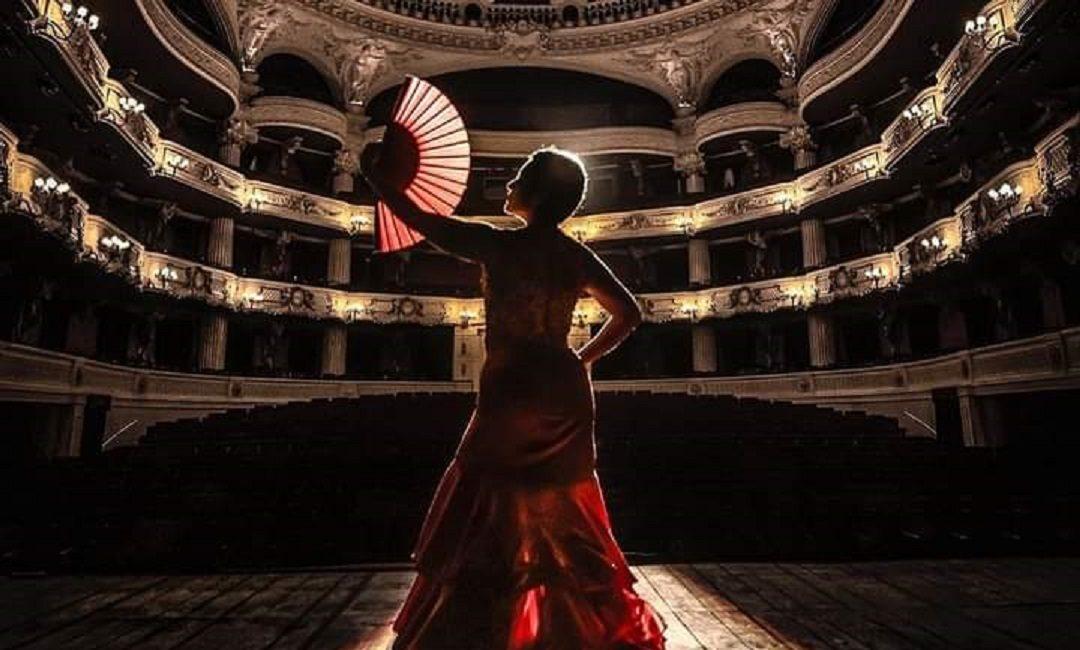 Bailarina en vestido rojo pivotando en el escenario del Teatro Municipal, con las galerías iluminadas de fondo