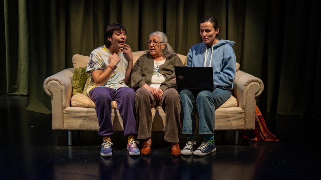 Cinco personas sentadas en un sofá beige sobre un escenario con cortina verde al fondo, en posición de panel