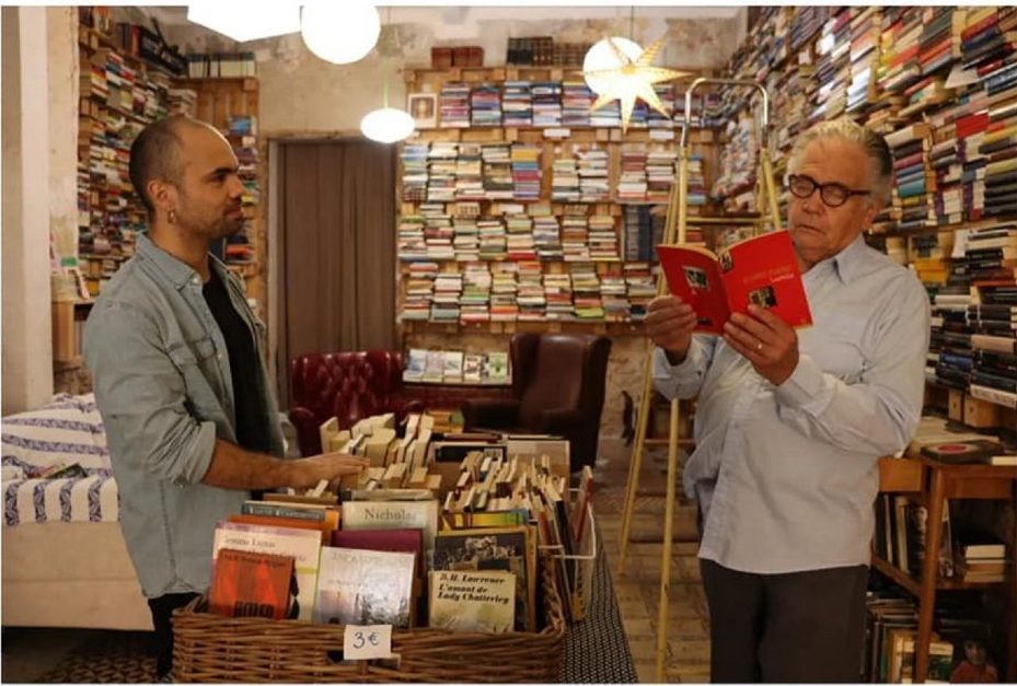 Edmundo Moure en librería conversa con otro hombre entre estanterías de libros de literatura