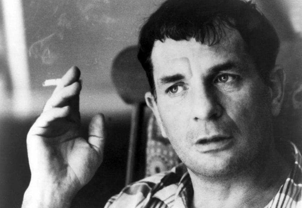 Jack Kerouac en blanco y negro, fumando, con expresión pensativa y la mano levantada, retrato de estudio