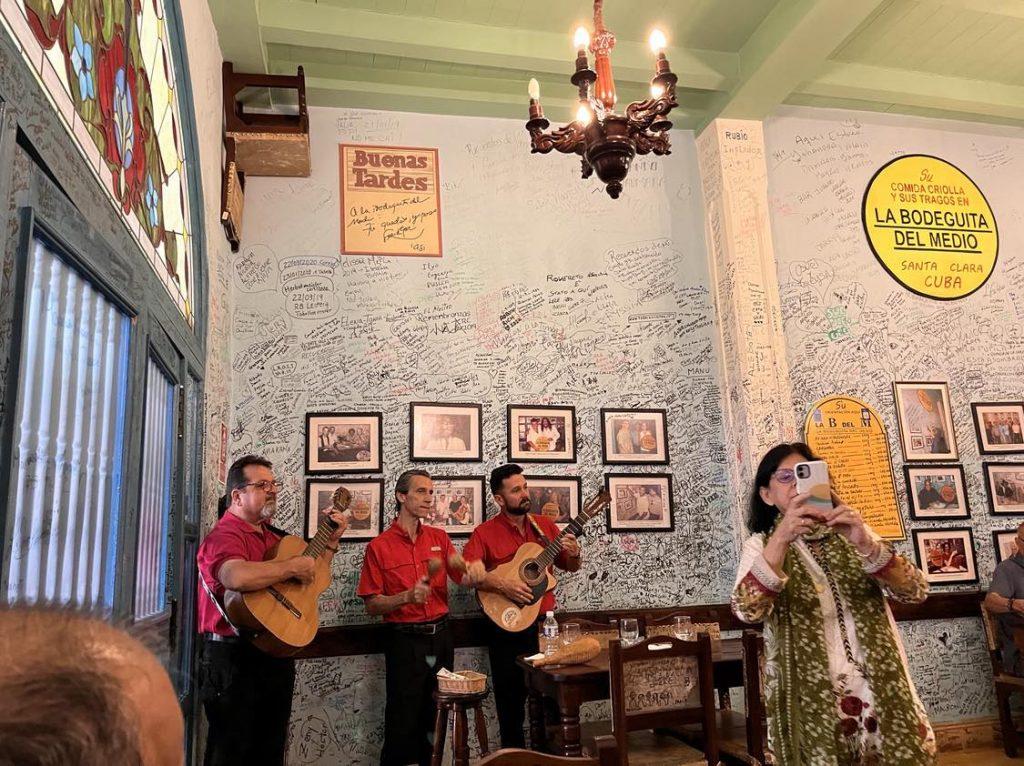Músicos y poeta en La Bodeguita del Medio durante Festival La isla en versos, con paredes decoradas con fotos y carteles