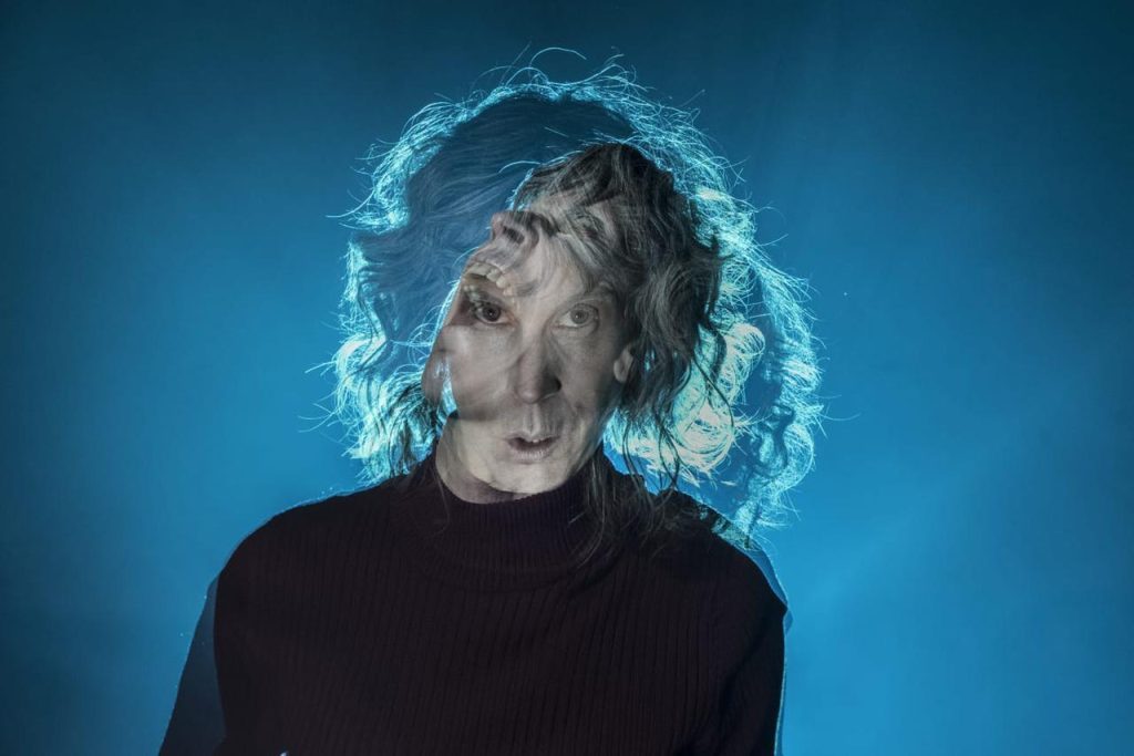 Hombre de mediana edad con cabello ondulado gris, expresión contemplativa, sobre fondo azul degradado con efecto de luz