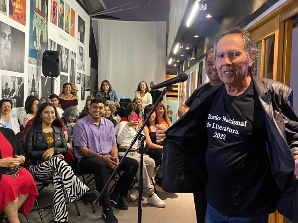 Hernán Rivera Letelier durante presentación en evento cultural con audiencia sentada en sala de cine