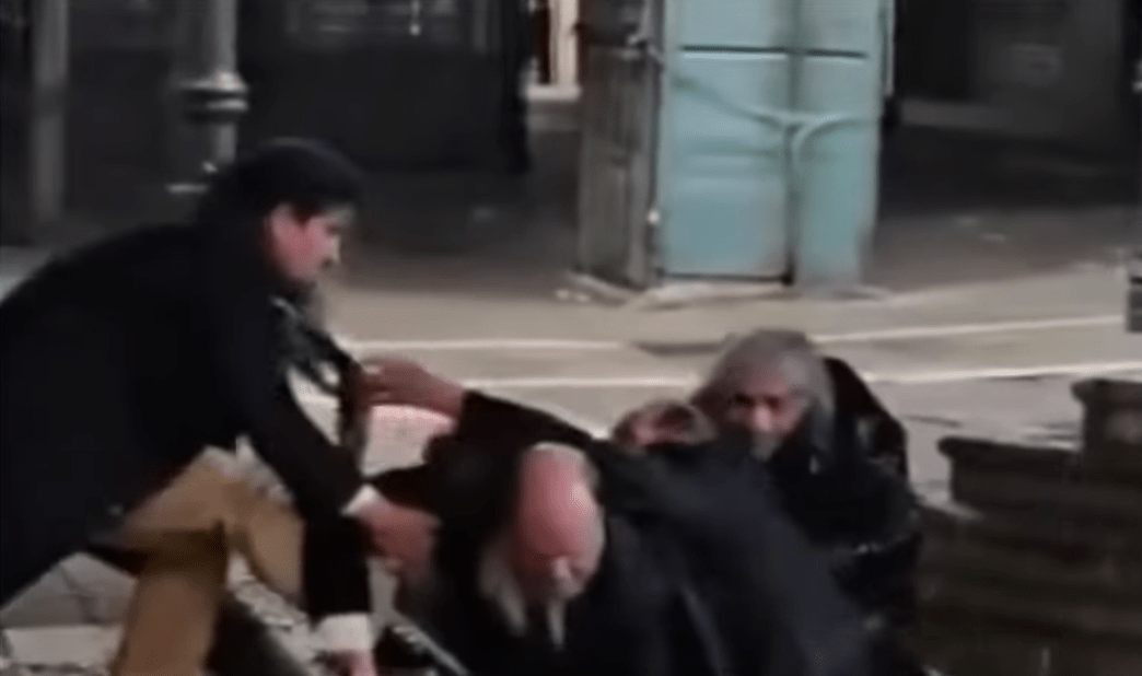 Dos hombres en pelea callejera, uno de ellos golpeando al otro en el suelo durante confrontación física en la calle