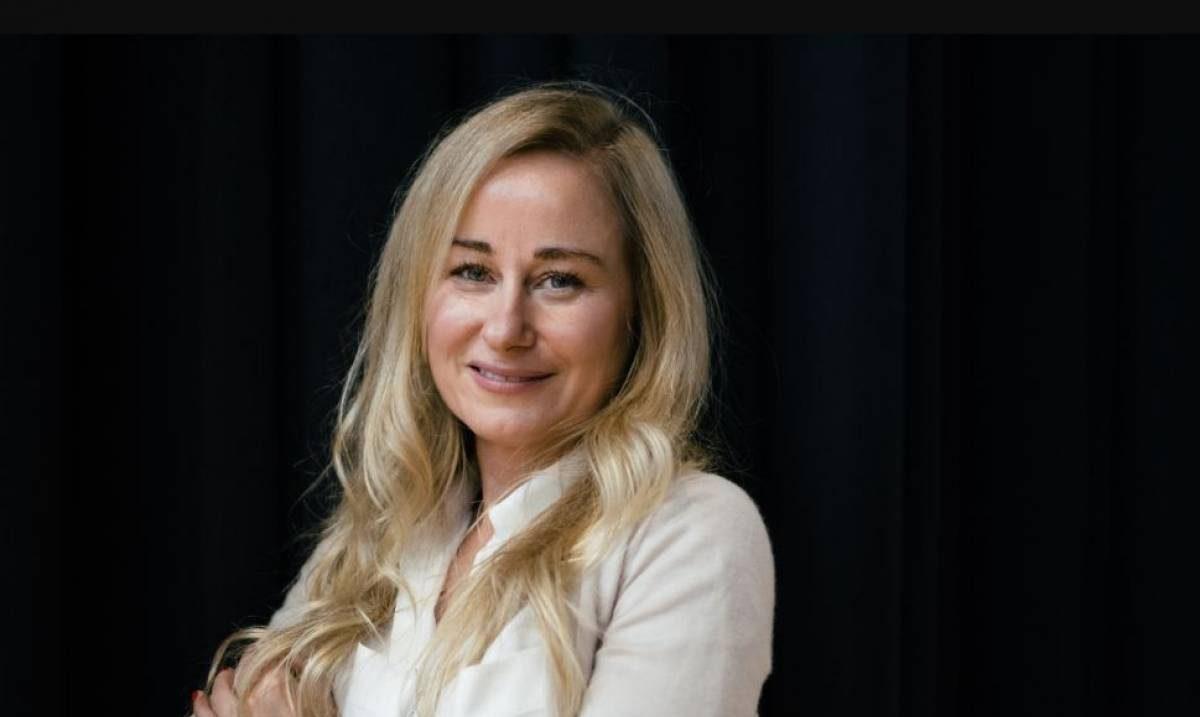Silvia Ferrara, mujer de cabello rubio largo, sonriendo hacia la cámara sobre fondo oscuro, vistiendo blusa blanca