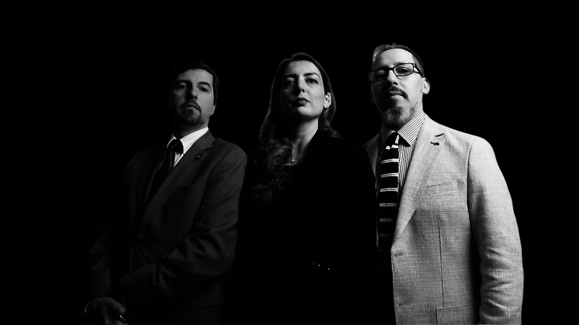 Tres hombres en blanco y negro contra fondo oscuro, postura seria y formal, retrato de autores