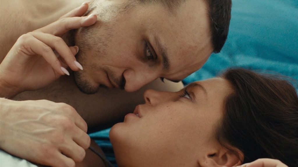Dos hombres besándose en primer plano con fondo azul turquesa en escena íntima de la película Passages