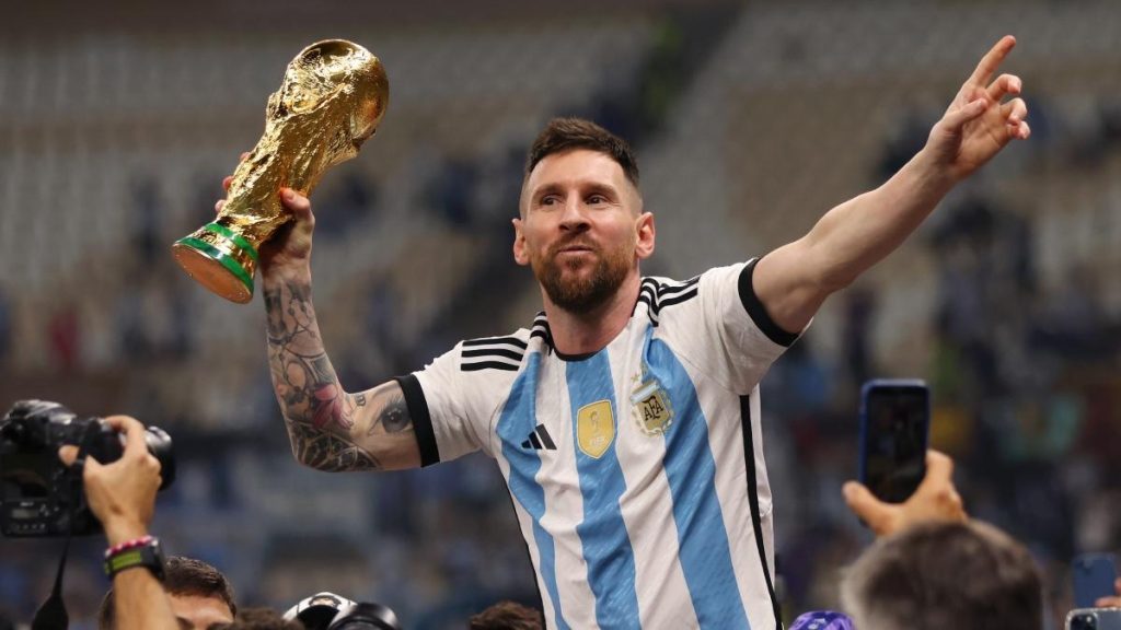 Lionel Messi sostiene la Copa Mundial con una mano levantada, vistiendo la camiseta argentina de rayas blancas y azules