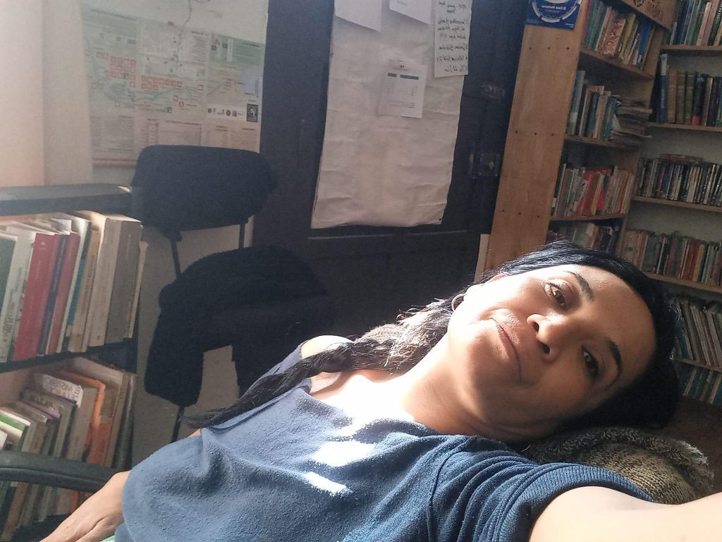 Patricia Ardiles recostada en un sofá negro dentro de una biblioteca, rodeada de libros y estanterías de madera