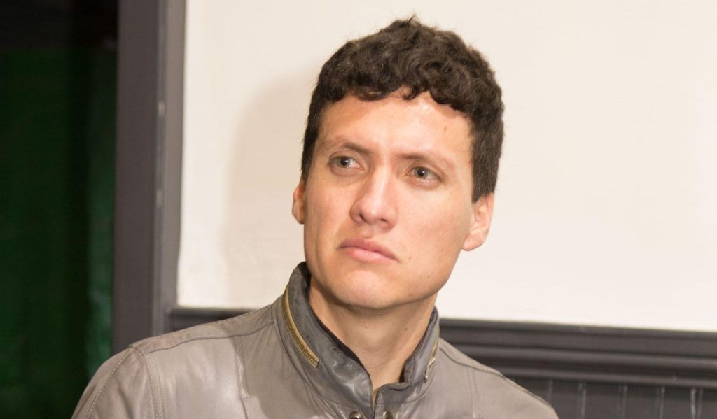 Esteban Catalán, hombre de cabello oscuro ondulado, viste camisa gris y mira hacia la cámara en ambiente de interior