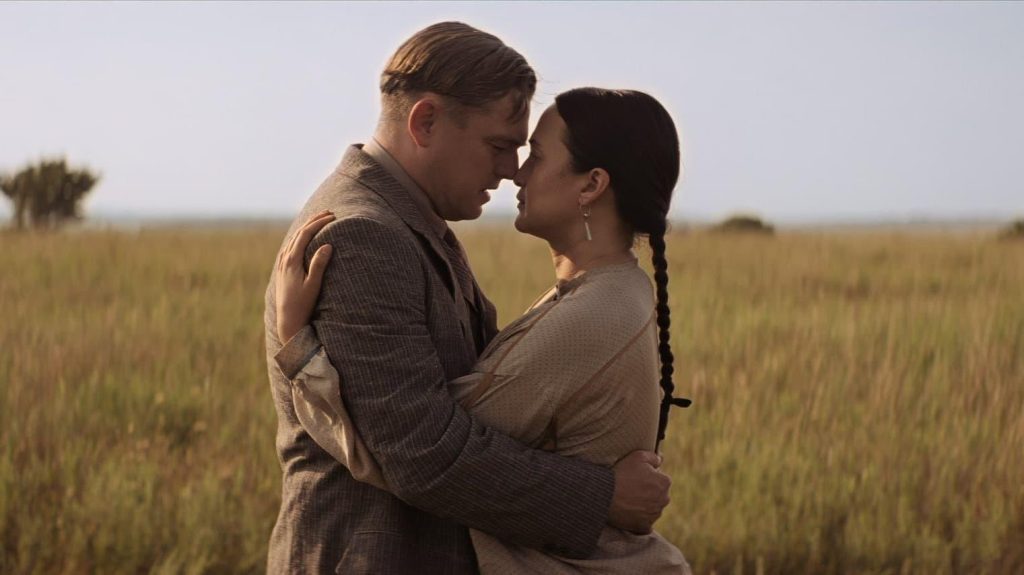 Pareja abrazándose en campo de hierba dorada al atardecer, escena de drama cinematográfico