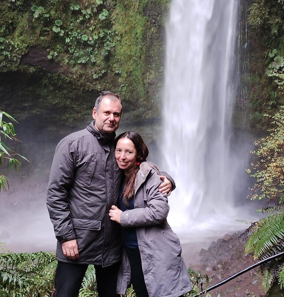 Pareja abraza junto a cascada en entorno de vegetación frondosa y rocas mojadas