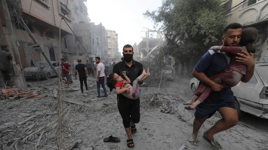 Hombres cargan niños entre escombros y ruinas de edificios destruidos en zona urbana devastada