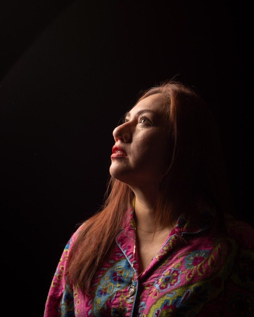 Mujer de perfil con cabello largo rojizo, mirando hacia arriba, usando blusa estampada en tonos magenta y azul