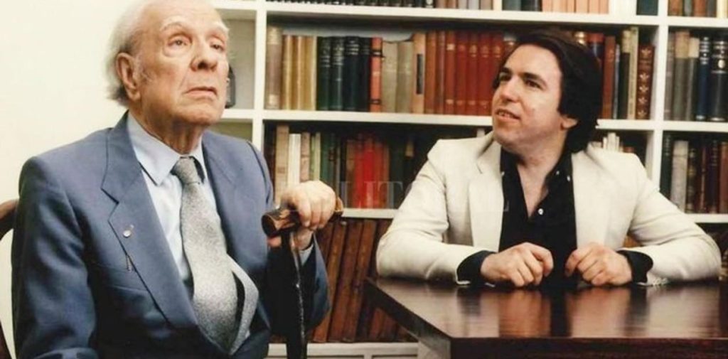 Jorge Luis Borges y Hector Ferrari en entrevista, sentados ante una mesa con biblioteca al fondo