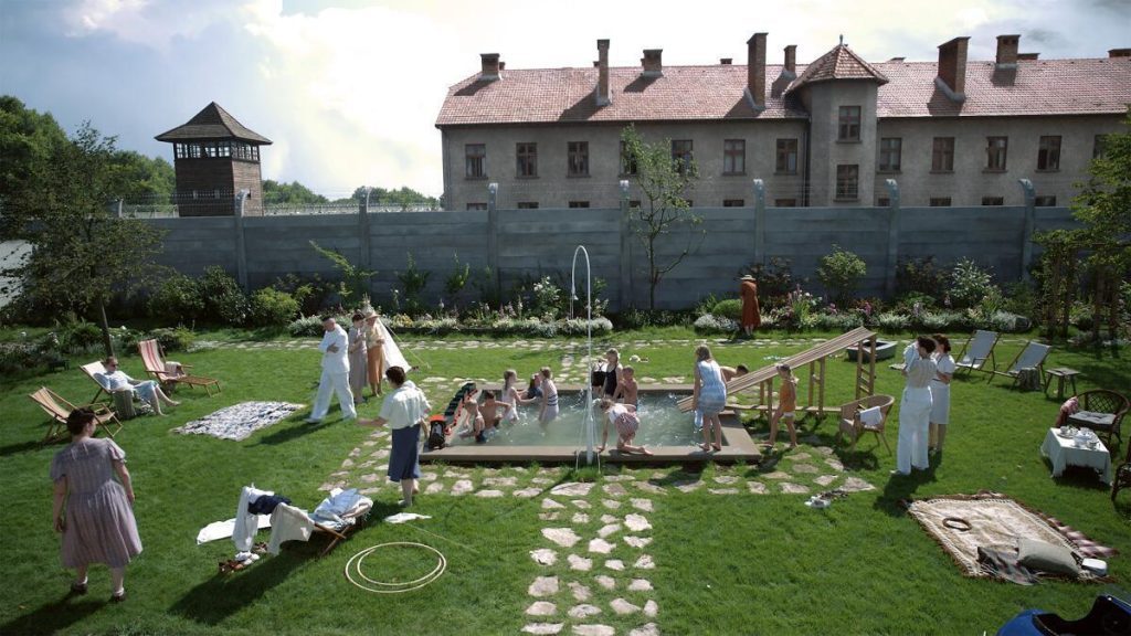 Ceremonia en jardín de mansión con asistentes vestidos de blanco interactuando alrededor de estructuras circulares
