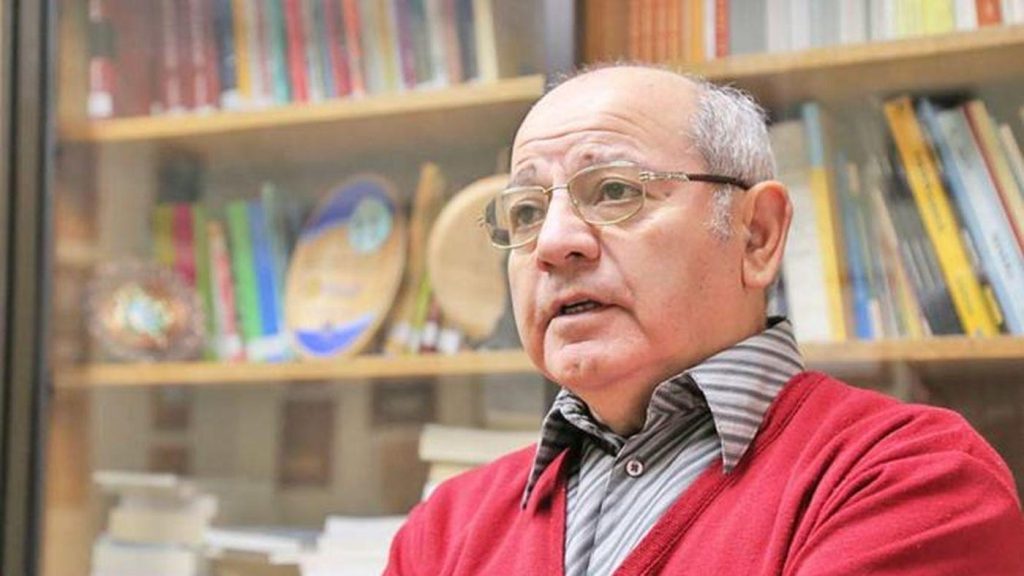 Rubén González Lefno, hombre mayor con anteojos y suéter rojo, en biblioteca con libros al fondo