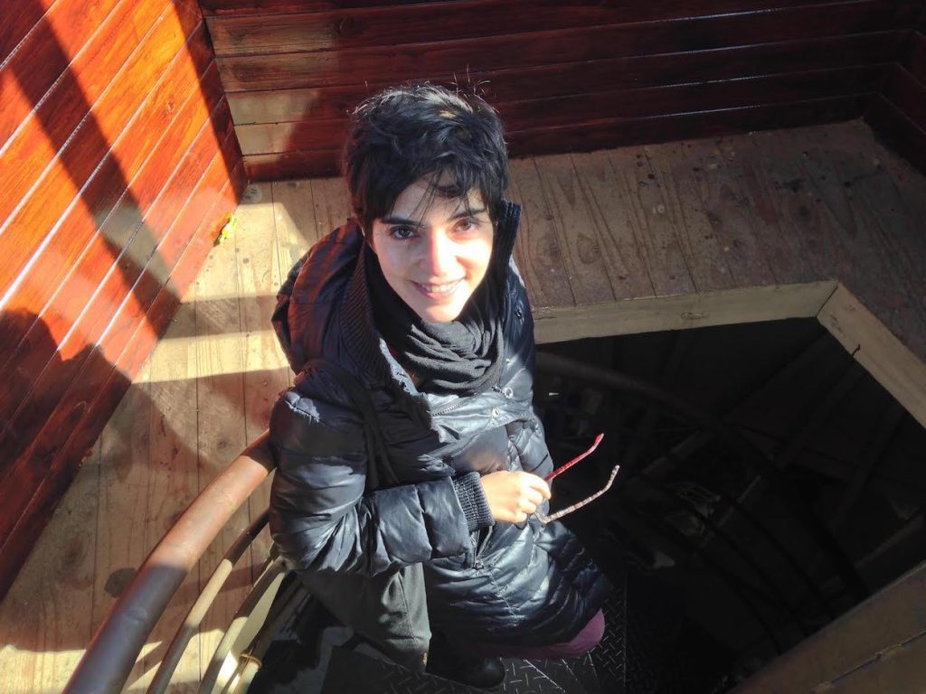 Mujer joven en interior con luz naranja, viste chaqueta negra y bufanda gris, mirada hacia cámara