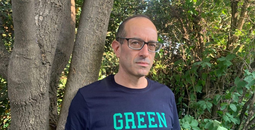 Nicolás Poblete, hombre con gafas y camiseta negra con texto verde, junto a árbol de fondo