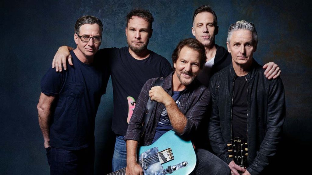 Cinco integrantes de Pearl Jam posando juntos en estudio, uno sostiene una guitarra azul claro