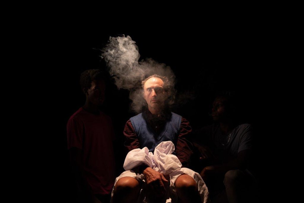 Personaje envuelto en humo denso sosteniendo una máscara de cerdo, con iluminación dramática sobre fondo oscuro